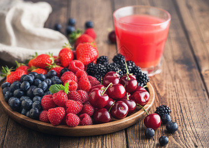 以圆木质盘装满果汁杯的圆木桌边盘中新鲜有机夏季果子混合物草莓蓝黑和樱桃顶部视图图片