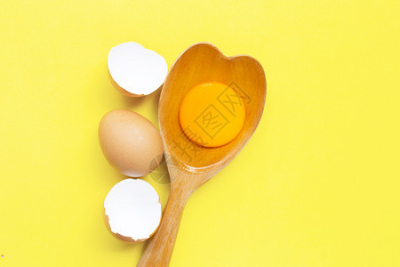 黄色背景的木勺心形上蛋和白顶部视图图片