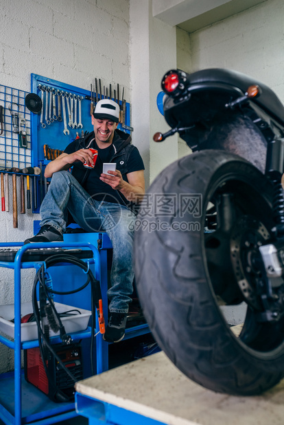 在他的车间里喝啤酒休息的摩托车修理工喝啤酒休息的摩托车修理工图片