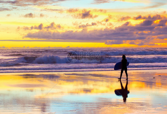 日落时冲浪者带着板在海滩上行走图片