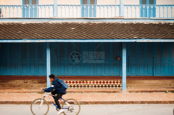 2019年4月日2019年卢昂普拉邦Laos蓝色门法国殖民地建筑和当小孩骑自行车在主要街道上图片
