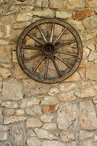 旧木制车轮挂在石头农舍墙上图片