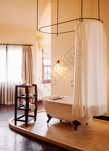 25daltvienam温暖气氛古老的殖民浴室用白色的倒向爪脚浴缸用白色的窗帘和木制边桌放在特拉兹佐地板上图片