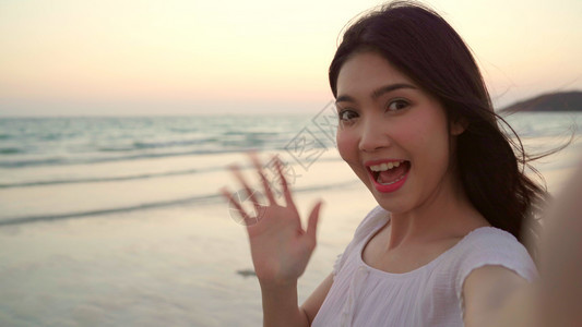 博客asinwom在海滩上录制vlog视频年轻美丽的女快乐使用手机在晚上日落时海边滩制作视频图片