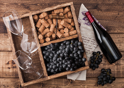 红酒瓶装在木头上空杯子黑葡萄软木塞和开瓶器装在旧木箱内质纸巾上图片