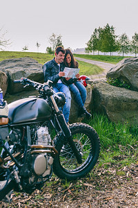 一对年轻夫妇骑摩托车旅行时坐在一起看一对夫妻骑着摩托车坐着看图片