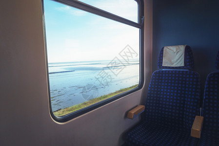 车内列窗边有一张蓝色的空椅子窗边有瓦登海景乘坐欣堡大坝前往锡尔特岛图片