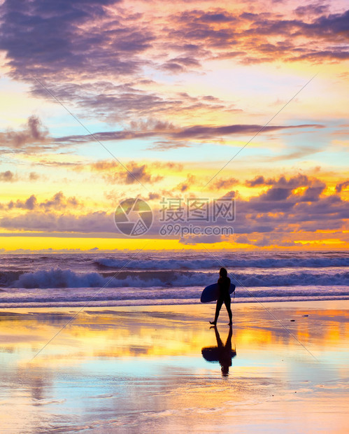 日落时冲浪者用板在海滩上行走图片