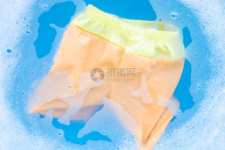黄色和橙婴儿短裤浸泡在洗衣清洁水溶解洗衣布蓝底概念中图片
