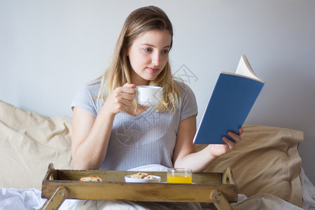 女人坐在床上看书吃早餐女孩上在房间里吃餐图片