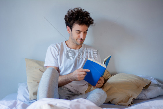 年轻拉丁男人躺在家里睡觉时读一本书图片