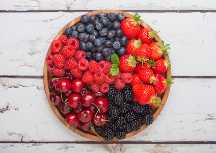 白木桌底的圆质盘中新鲜的有机夏季果子混合物草莓蓝黑和樱桃顶部视图图片