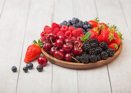 浅木制桌底的圆质盘中新鲜的有机夏季果子混合物草莓蓝黑和樱桃图片