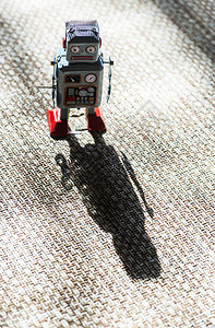 古老的金属蓝色机器人在阳光下的玩具与小型机械器人玩具在布面上行走的远期概念涂漆的眼睛和电子仪表板机械玩具钥匙硬光和阴影图片