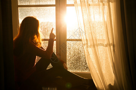 女孩坐在窗台上看着夜晚的城市橙色夕阳的光束图片