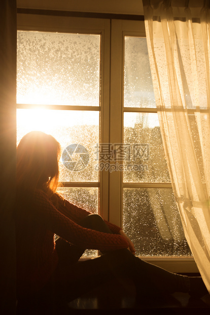 女孩坐在窗台上看着夜晚的城市橙色夕阳的光束图片