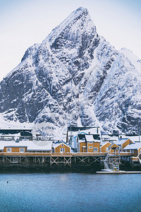 传统的挪威木制屋站在峡湾的岸边和远处山上岛屿北部图片