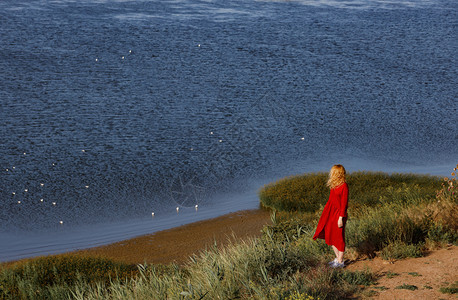 穿着红裙子的女人在日出时沿着海岸行走图片