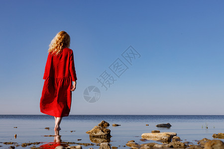 穿着红色长裙的金发女郎早上站在大海里图片