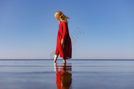 穿着红色长裙的金发女郎早上站在大海里图片