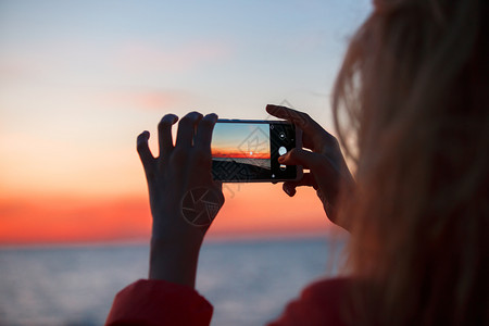 女旅行者使用智能手机拍摄多彩的海日落照片女旅行者使用智能手机拍摄多彩的海日落照片图片