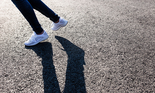 穿着白色运动鞋的女子在日落时沥青路上向日落时晒在沥青路向日晒在沥青路向日晒图片
