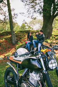 与年轻夫妇一起在背景中休息的摩托车旅行中自定摩托车有选择地关注前方的摩托车与年轻夫妇一起自定摩托车图片