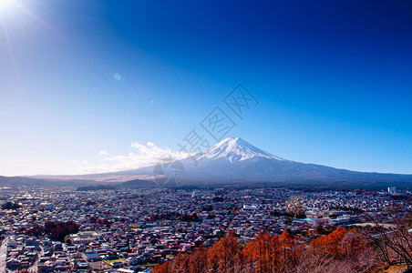 在河口谷附近的fujiyoshda公园中看到有雪和蓝天太阳耀斑的fuji山有彩色秋树和香木的Shimoysda城市在川口果附近的图片