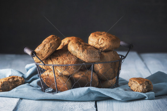 蓝厨房毛巾上的铁篮子里新鲜烤黑麦面包篮子里的热面包卷健康的自制面包图片