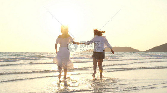 年轻女夫妇在海滩上奔跑美丽的女朋友很高兴在晚上日落时海边滩玩得开心图片