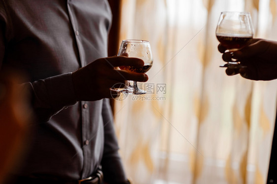 朋友站在窗边手握着装有威士忌的杯子图片