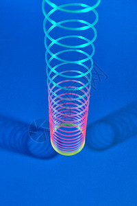 蓝色背景以上挂着多彩的塑料弹簧玩具表面有两个阴影复制空间垂直伸展的塑料弹簧玩具与两个阴影图片
