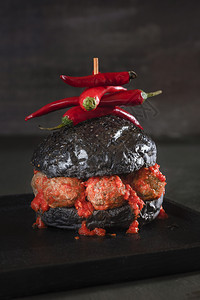 黑面包汉堡有肉丸和辣番茄酱在黑盘和桌子上浅的奇异汉堡形象怪的食物圣餐图片