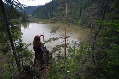 夏季公路旅行带智能手机的女孩在山湖拍照图片
