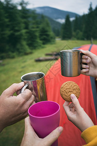 女孩和男徒步旅行者在山上帐篷的背景拿着杯子和饼干图片