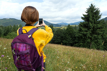 带着背包和智能手机的旅游女孩站在山上的草地图片