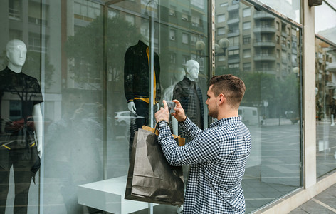 年轻男子在时装店的商窗户上拍摄一名模特男的照片子在时装店商窗户上拍摄了一张时装店窗户的照片图片