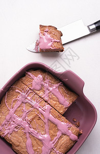 红宝石巧克力蛋糕放在粉红色的托盘里和刀上的一部分在白桌上的粉红色布朗尼上方平整的巧克力蛋糕粉红色的甜点图片