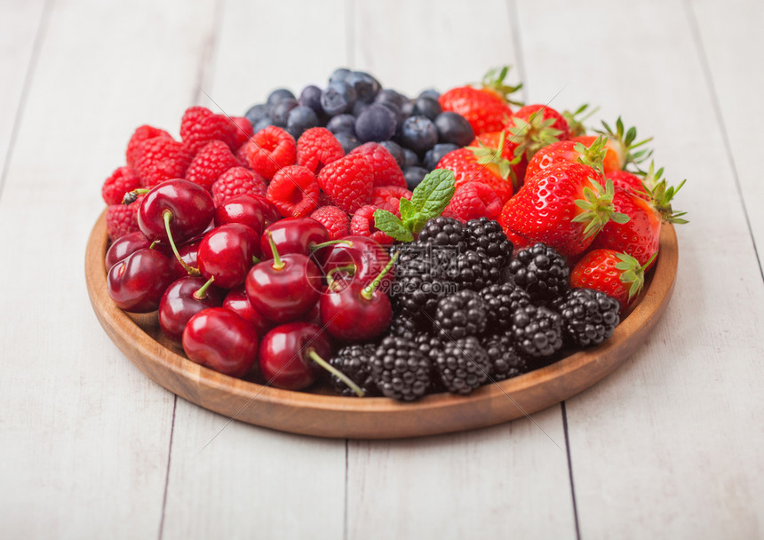 浅木制桌底的圆质盘中新鲜的有机夏季果子混合物草莓蓝黑和樱桃图片