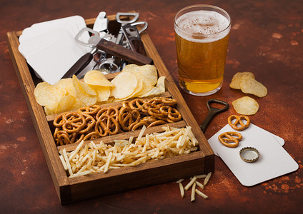 棕色厨房餐桌背景上装着一盒零食的杯式啤酒和开瓶器图片