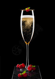高雅的黄色香槟杯子上面有彩虹和新鲜的浆果还有黑大理石板上粘着薄荷叶的图片