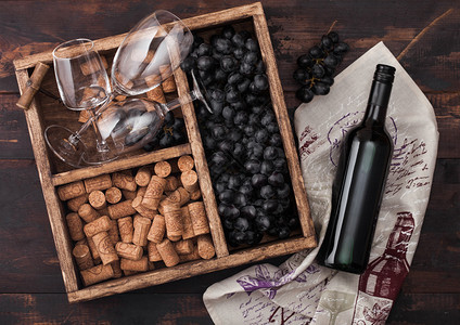 木头上装满空杯子的红酒瓶黑葡萄装有软木塞和用黑色质的盒子底装有纸巾图片