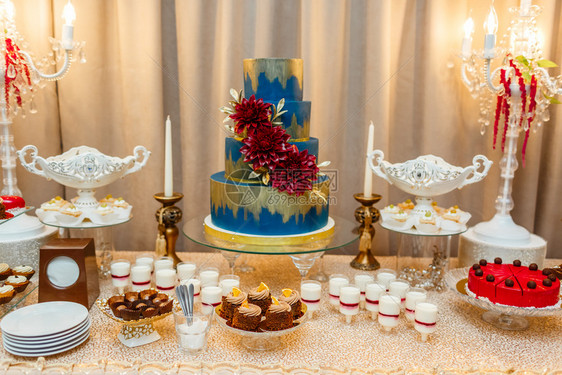 蓝色婚礼蛋糕由盛宴桌边的花朵和沙漠草莓薄饼和蛋糕婚礼接待薄饼糖果棒图片