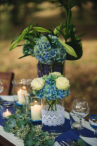 在树林的木制板上有花朵安排蓝色白绿花朵和蜡烛雕塑玻璃餐具照片贴近装饰细节在树林的木制板上有蓝色绿花朵和餐具背景图片