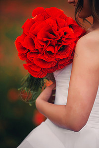 穿着白色婚纱的女孩手上拿着红花在的背景下夏天穿着白色婚纱的女孩在红花背景下图片