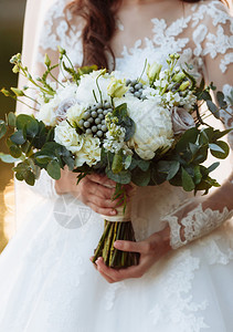 身着优雅礼服的年轻美女站着手拿鲜花和带丝的鲜花和绿色新娘在户外举行婚礼花束图片