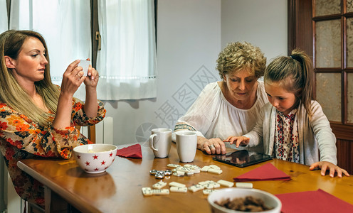 外祖母和孙女在桌子上玩平板小游戏妈妈用手机给她们拍照图片