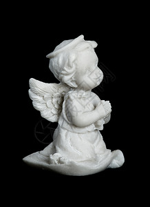 一个小男孩的雕塑或像翅膀天使手折在祈祷中孤立黑色背景上图片