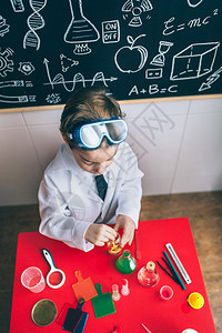 小男孩科学家在桌子上玩化学液体与带图画的黑白板对着桌子上玩化学液体图片