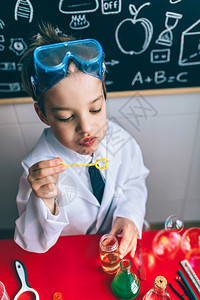 小男孩科学家的肖像坐在桌边玩肥皂泡与抽黑板比对图片